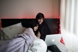 couple on bed using MacBook Air beside of window with white curtain