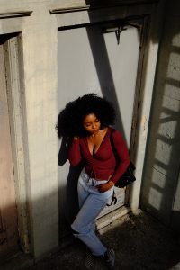 woman in red long sleeve shirt and blue denim jeans leaning on wall