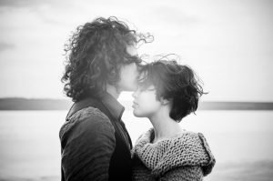 grayscale of man kissing woman's forehead