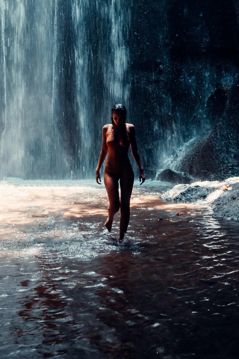 woman in black bikini standing on water falls during daytime