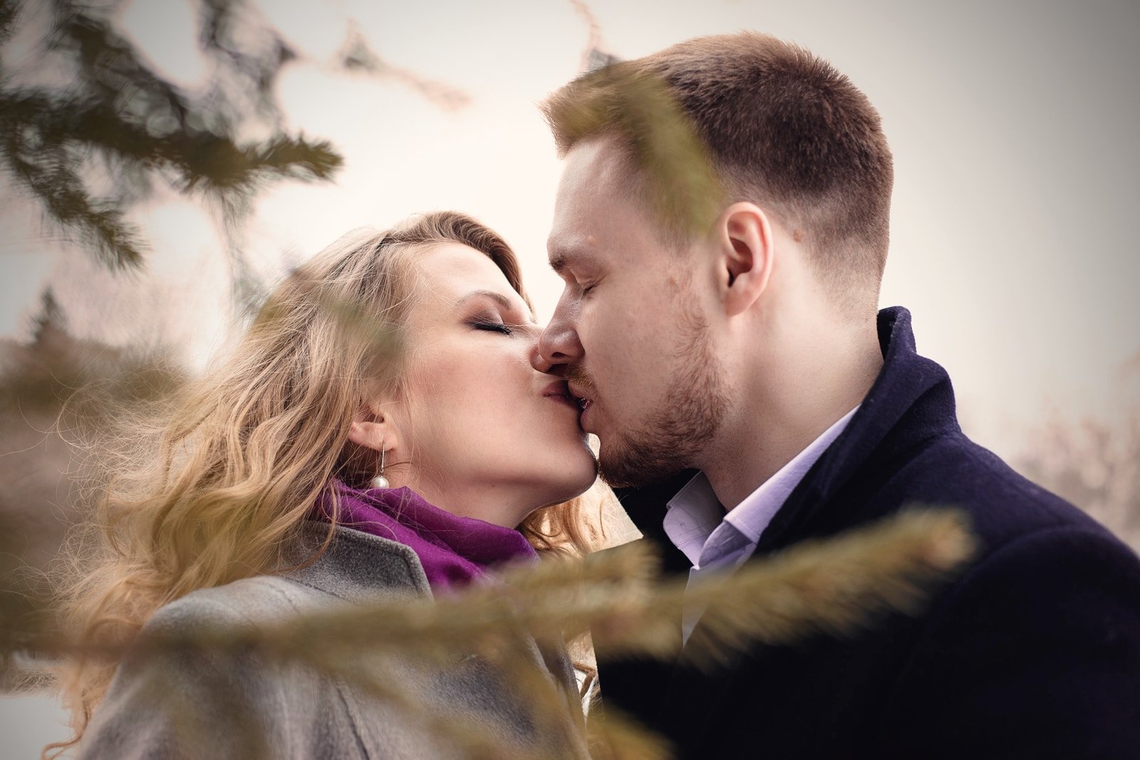 man and woman kissing near green leafed tree