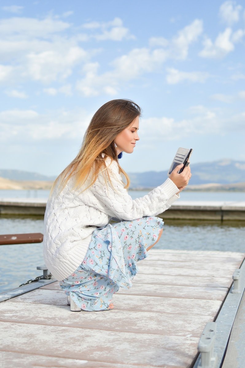 woman using smartphone while sitting of dock during daytime