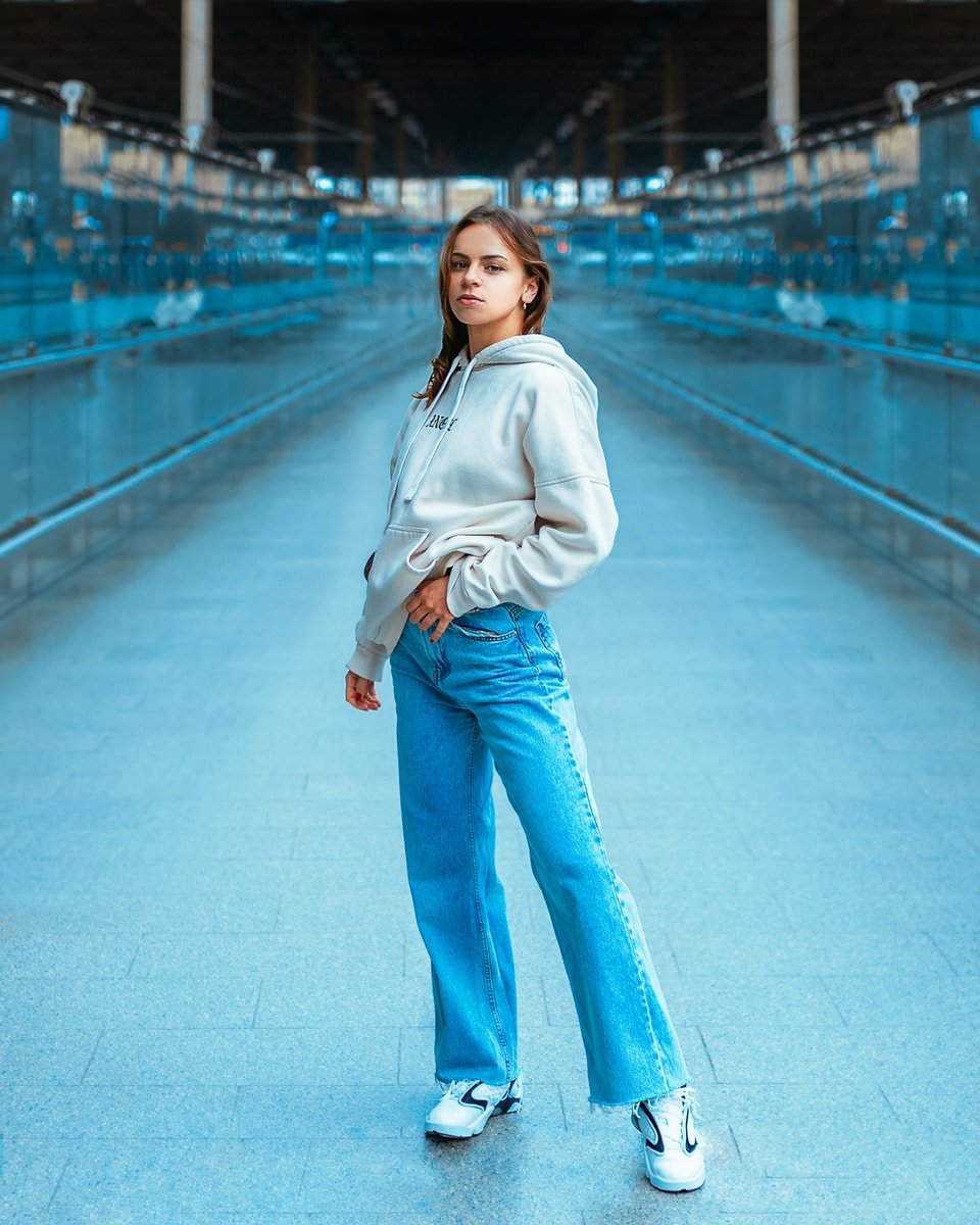 woman in white hoodie and blue denim jeans standing on bridge